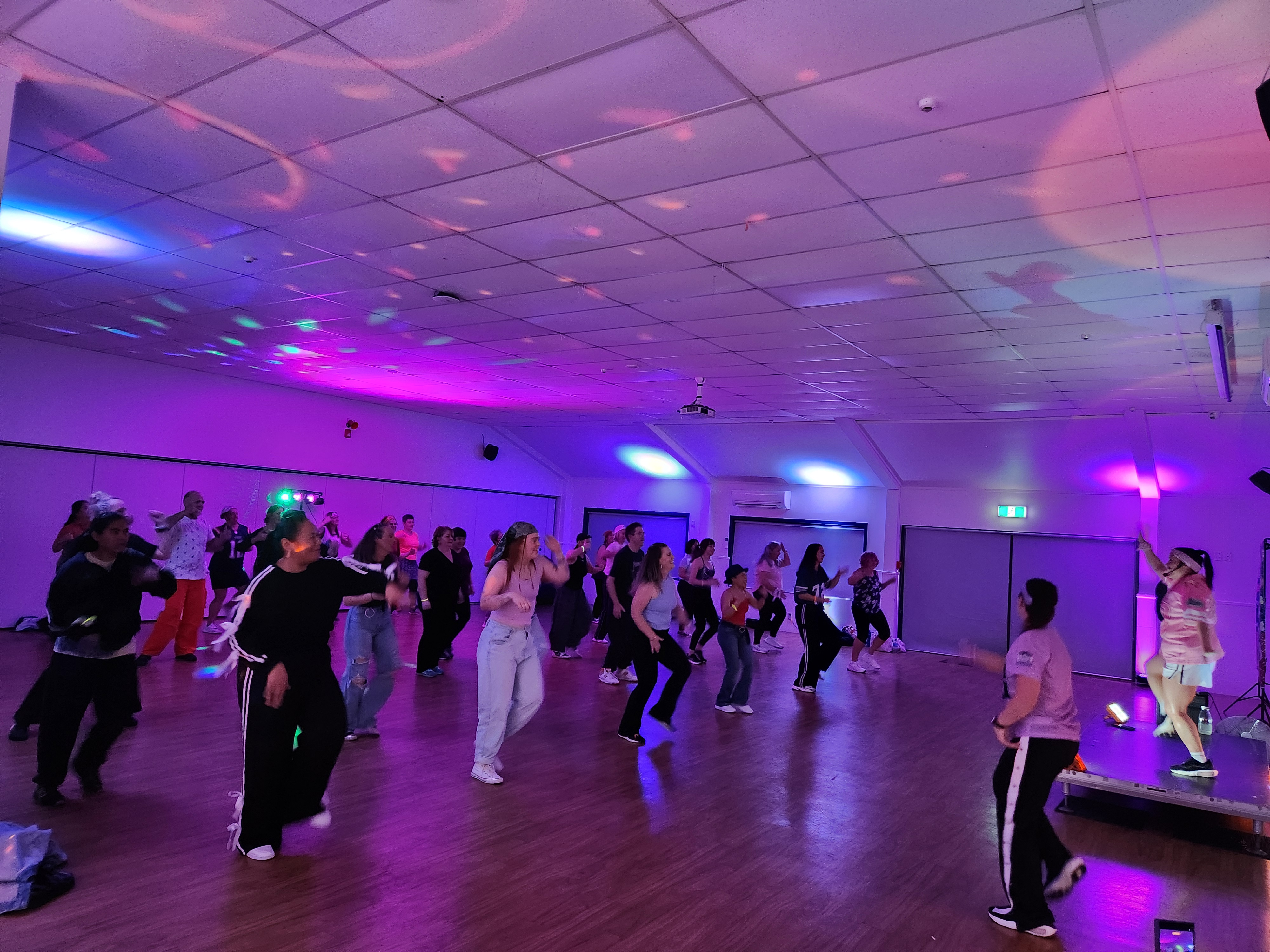 A packed Dance Fit with Jen class moving together under pink and purple disco lights